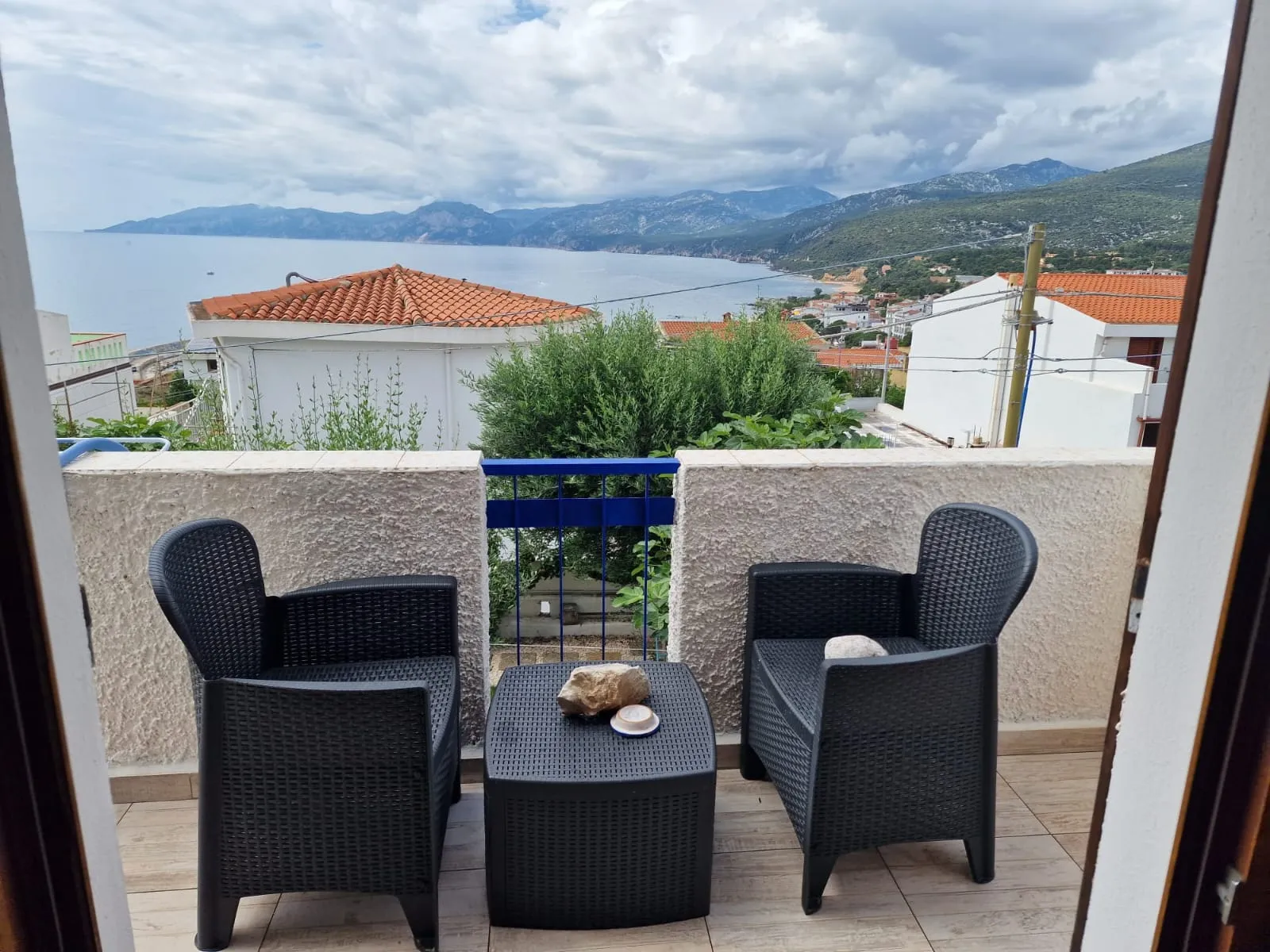 Balcone privato della camera Cala Goloritzè con due poltroncine in rattan nero e vista sui tetti, sul mare e sui monti del Golfo