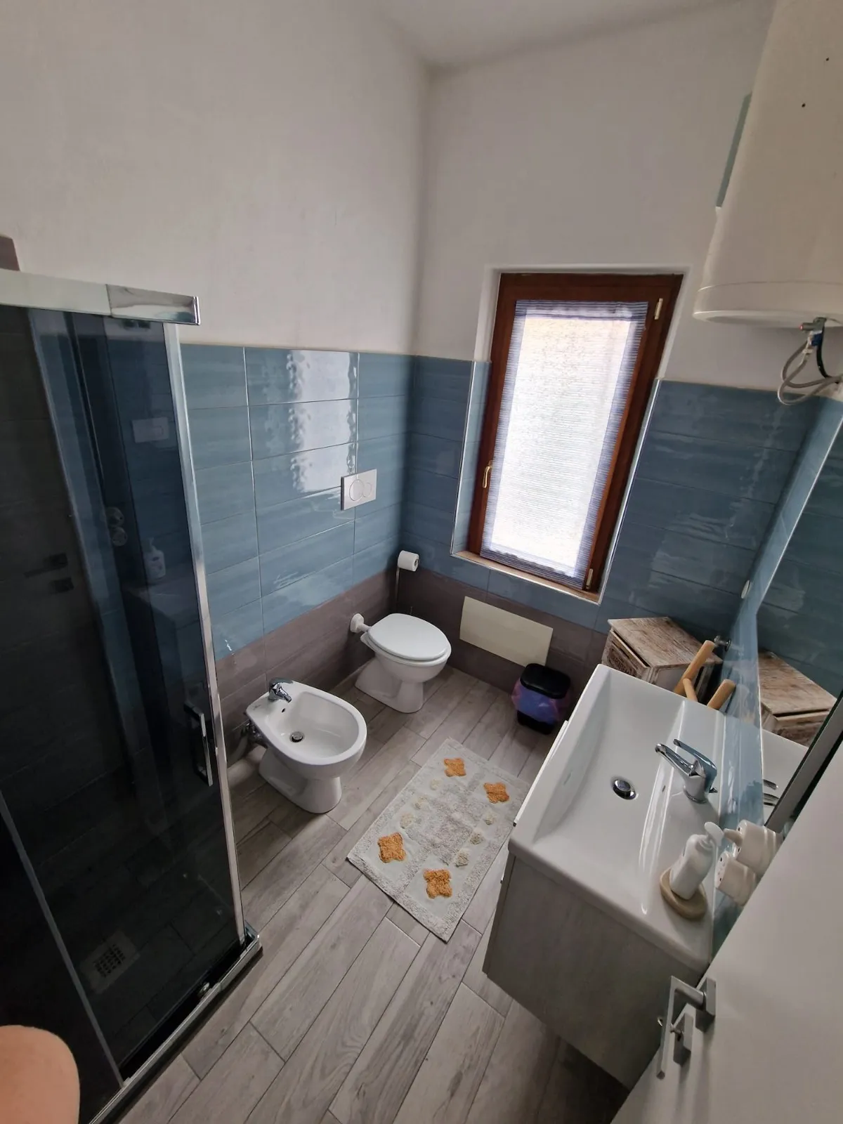 Bagno privato della camera Monte Litty con piastrelle azzurre lucide, box doccia in vetro scuro e mobile con lavabo