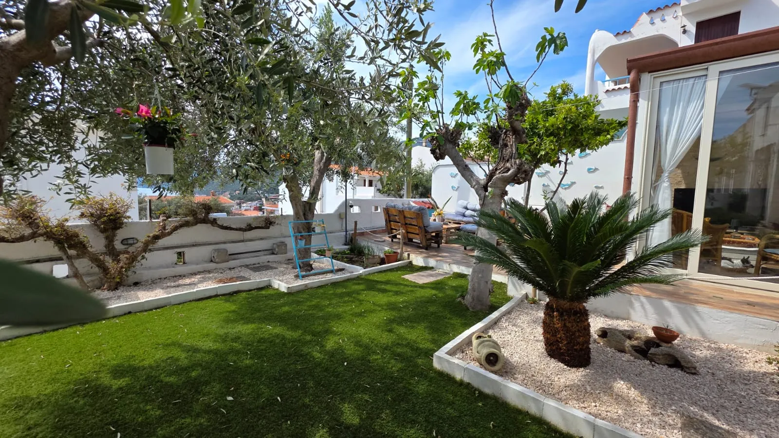 Il giardino del B&B con l’ulivo sul prato, la palma, i bordi in ghiaia bianca e la veranda a vetri
