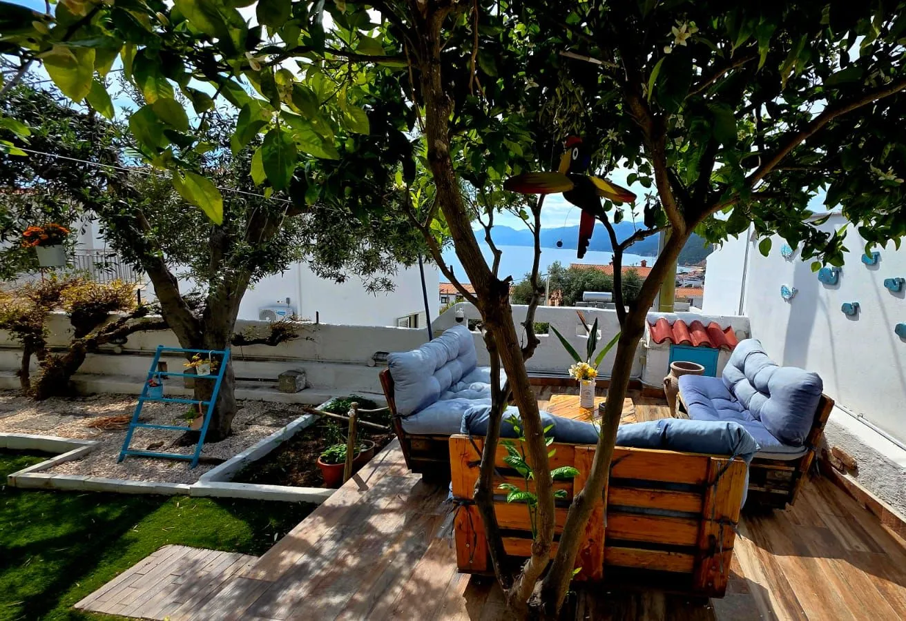 La terrazza panoramica del B&B con i divani in pallet sotto gli alberi, la vista su mare e monti e il giardino a fianco
