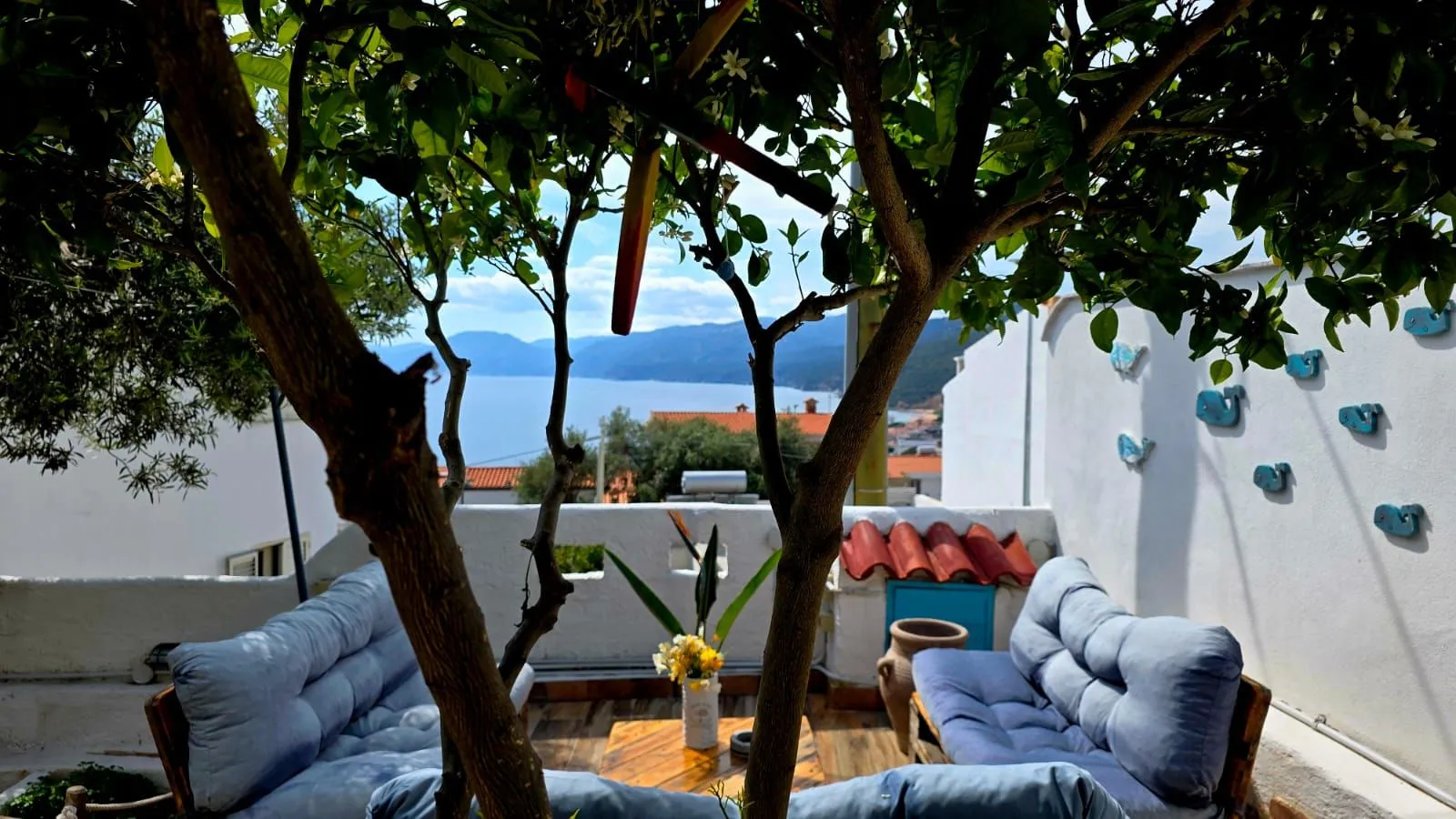 La terrazza con i divani in pallet e i cuscini azzurri incorniciati dagli alberi, le balene decorative sul muro bianco e la vista sul mare del Golfo
